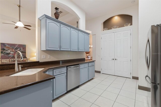 kitchen featuring light tile patterned floors, a ceiling fan, blue cabinetry, a sink, and appliances with stainless steel finishes