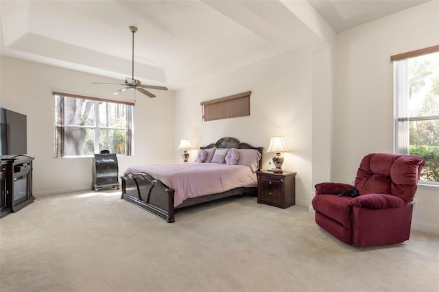 bedroom featuring a tray ceiling, multiple windows, and light colored carpet