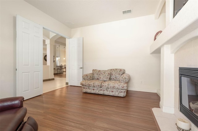 living room with a tiled fireplace, wood finished floors, arched walkways, and visible vents