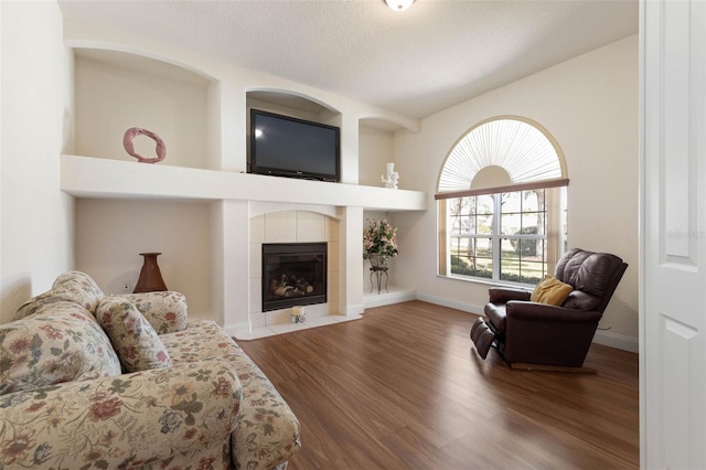 living room featuring a tiled fireplace, wood finished floors, baseboards, and a textured ceiling