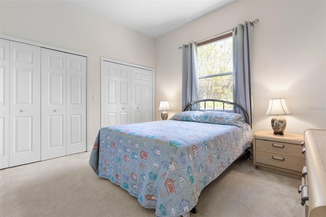 bedroom featuring light colored carpet and multiple closets