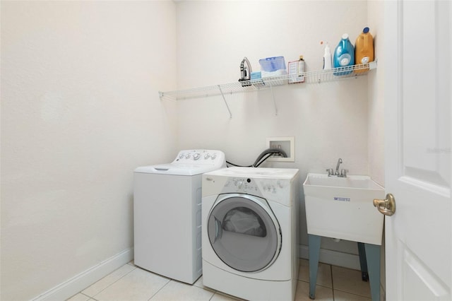 laundry area with baseboards, light tile patterned floors, laundry area, separate washer and dryer, and a sink