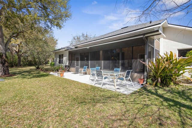 rear view of property with a yard, a sunroom, stucco siding, and a patio area