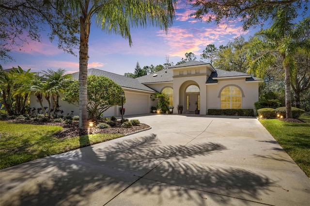 mediterranean / spanish-style house with stucco siding, an attached garage, concrete driveway, and roof with shingles