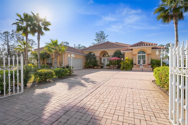 mediterranean / spanish house with decorative driveway, a tiled roof, an attached garage, and stucco siding