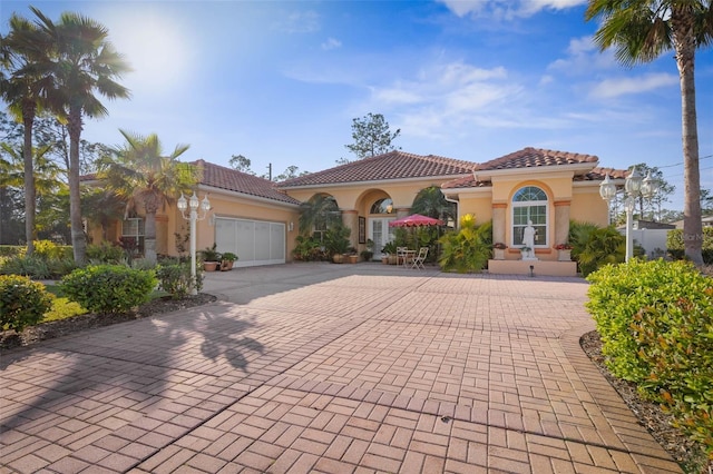 mediterranean / spanish-style home featuring a garage, a tiled roof, decorative driveway, and stucco siding