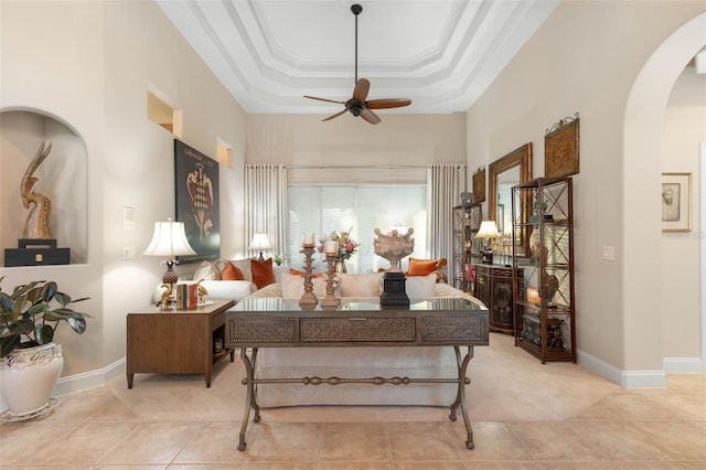 living area featuring arched walkways, crown molding, a raised ceiling, a ceiling fan, and tile patterned floors