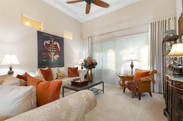 carpeted living room with ceiling fan, a raised ceiling, and a towering ceiling