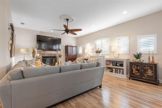 living room with light wood-style flooring, recessed lighting, a ceiling fan, visible vents, and a glass covered fireplace