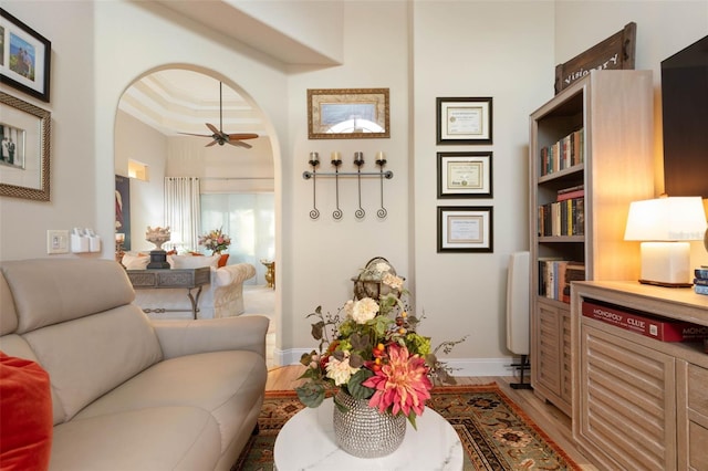 living area featuring light wood-style flooring, baseboards, a ceiling fan, and ornamental molding