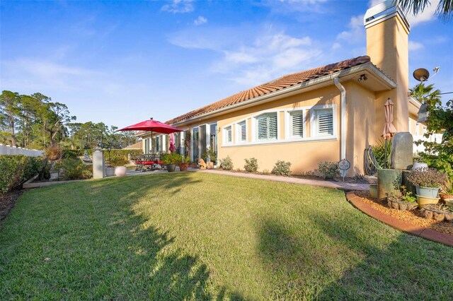 back of house with a patio, a tile roof, a lawn, stucco siding, and a chimney