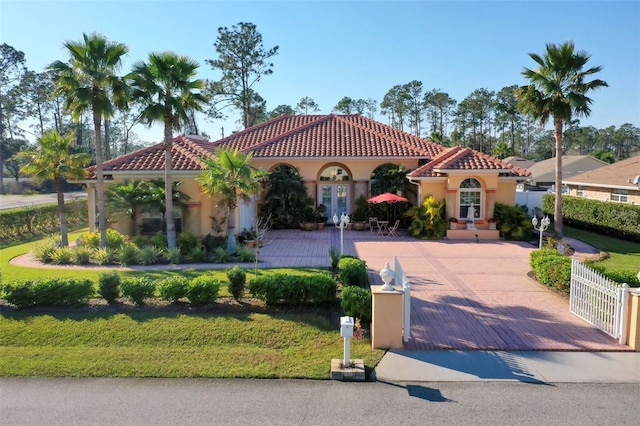 mediterranean / spanish house featuring a fenced front yard, decorative driveway, french doors, a tile roof, and stucco siding