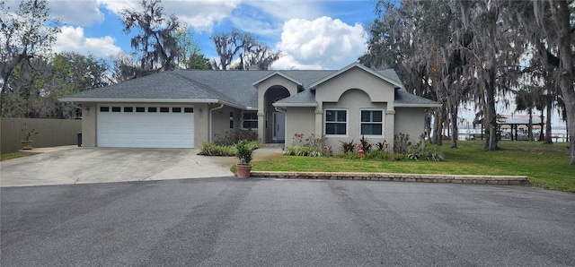 single story home featuring stucco siding, an attached garage, a front yard, fence, and driveway