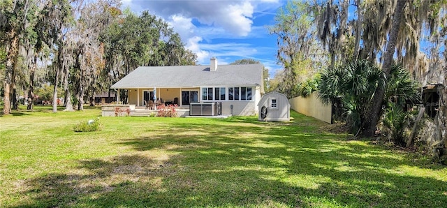 rear view of property featuring an outbuilding, a chimney, a lawn, a patio area, and a shed