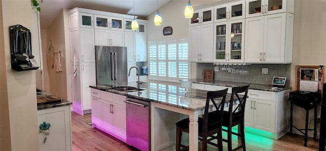 kitchen featuring white cabinets, a sink, stainless steel appliances, light wood-type flooring, and backsplash