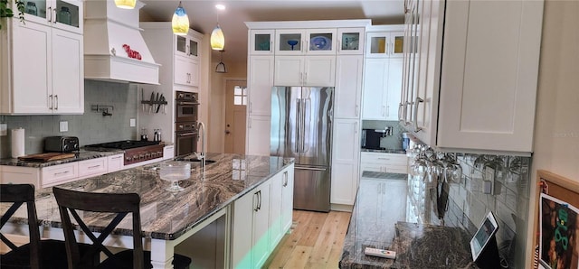 kitchen featuring light wood-style flooring, decorative backsplash, appliances with stainless steel finishes, white cabinets, and dark stone countertops