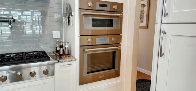 kitchen with white cabinets, light stone countertops, stainless steel appliances, and backsplash