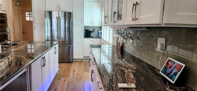 kitchen with backsplash, glass insert cabinets, freestanding refrigerator, white cabinetry, and light wood-type flooring