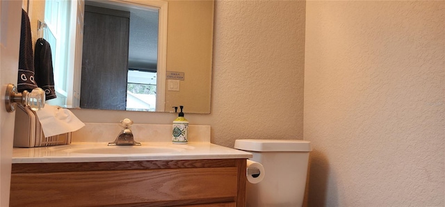 bathroom featuring toilet, vanity, and a textured wall