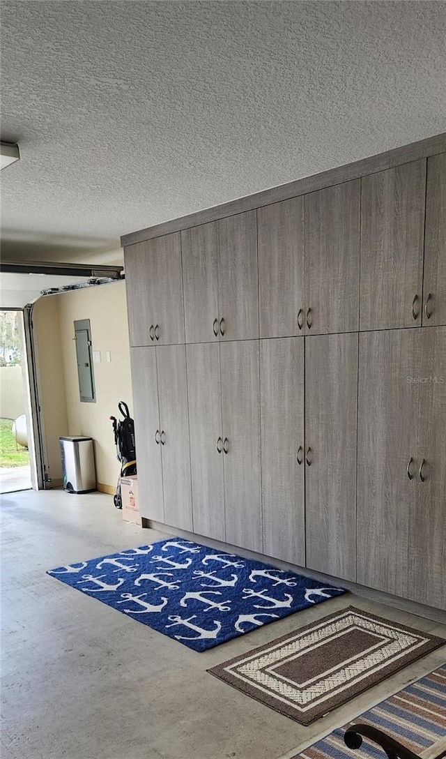 interior space with a garage, electric panel, access to exterior, concrete flooring, and a textured ceiling