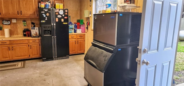 kitchen with brown cabinetry, light countertops, concrete flooring, and black fridge with ice dispenser