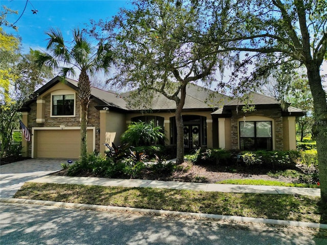 view of front of house with decorative driveway, stone siding, an attached garage, and stucco siding