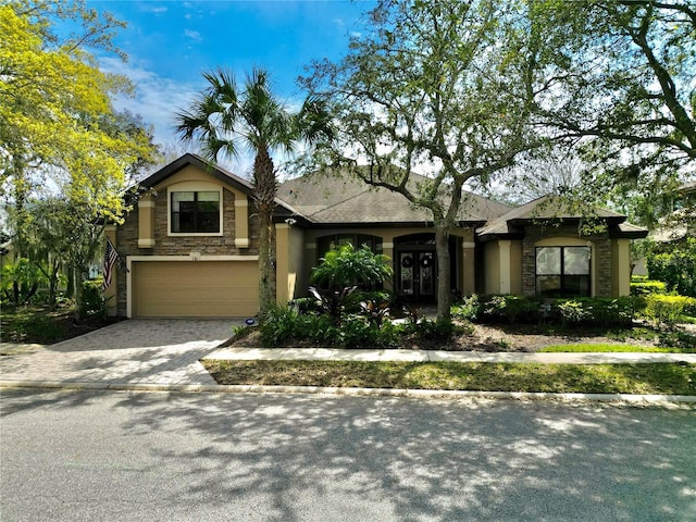 view of front of home featuring a garage, stone siding, french doors, decorative driveway, and stucco siding