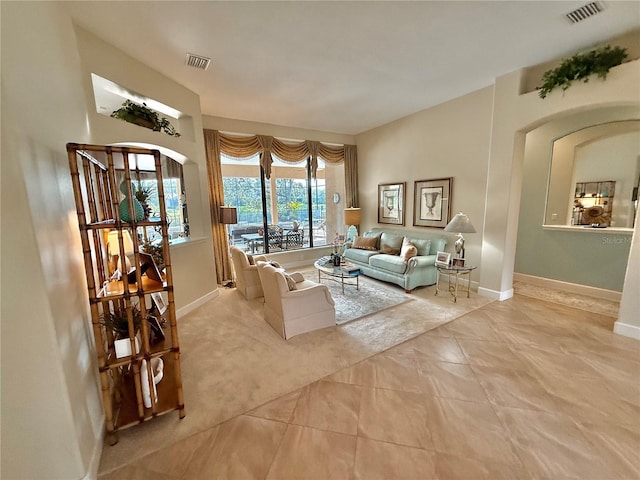 carpeted living area featuring tile patterned flooring, visible vents, arched walkways, and baseboards