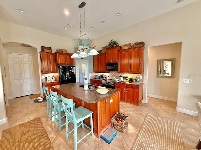 kitchen featuring arched walkways, a breakfast bar area, backsplash, black appliances, and an island with sink