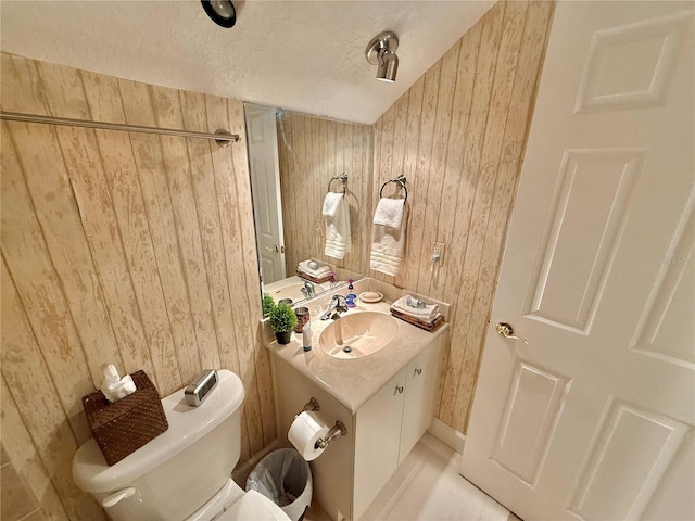 bathroom featuring a textured ceiling, toilet, wood walls, and vanity