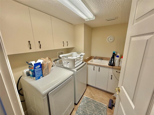 washroom with cabinet space, light tile patterned floors, washer and clothes dryer, a textured ceiling, and a sink