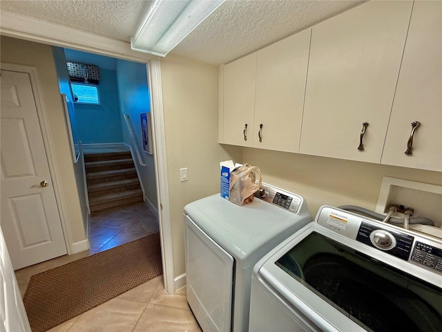 laundry area featuring washer and dryer, cabinet space, a textured ceiling, and light tile patterned floors