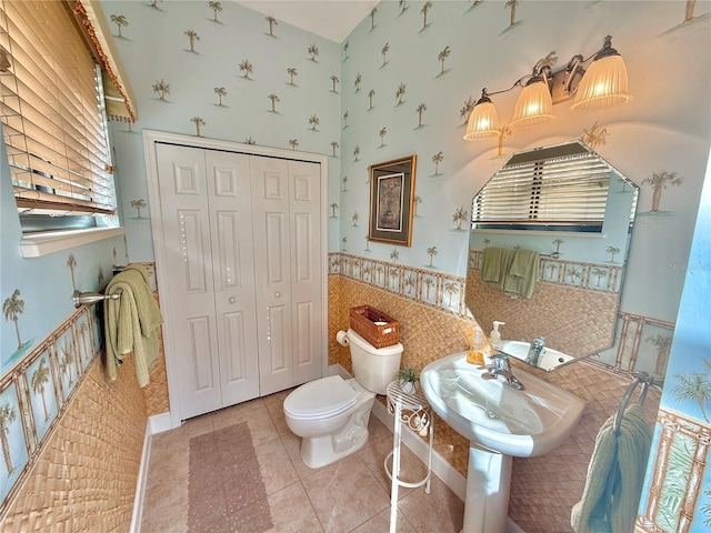 bathroom with wallpapered walls, toilet, a wainscoted wall, tile patterned flooring, and a closet