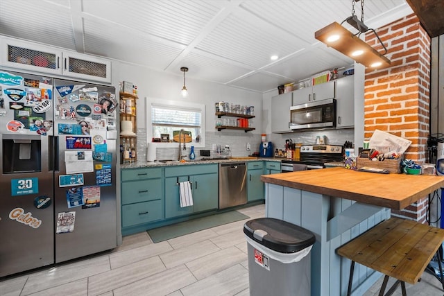 kitchen with tasteful backsplash, appliances with stainless steel finishes, a peninsula, a kitchen bar, and wooden counters