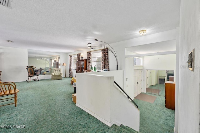 hall with carpet flooring, visible vents, an upstairs landing, and a textured ceiling