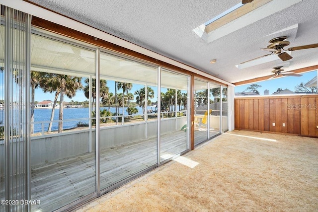 unfurnished sunroom with a water view, vaulted ceiling with skylight, and a ceiling fan