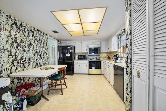 kitchen featuring light countertops, visible vents, a sink, black appliances, and wallpapered walls