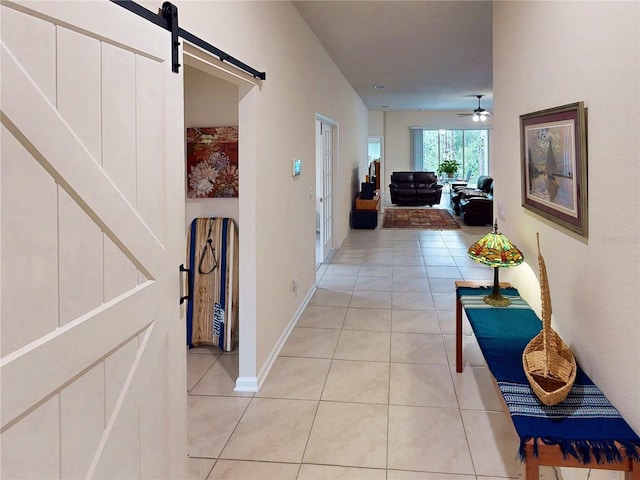 corridor featuring light tile patterned flooring, baseboards, and a barn door