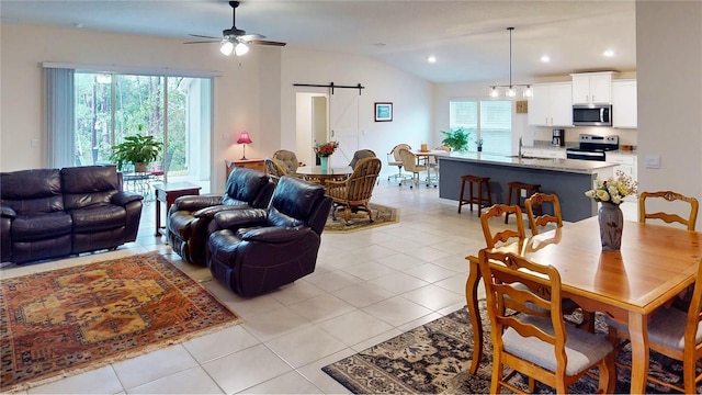 living area featuring vaulted ceiling, a barn door, light tile patterned flooring, and a healthy amount of sunlight