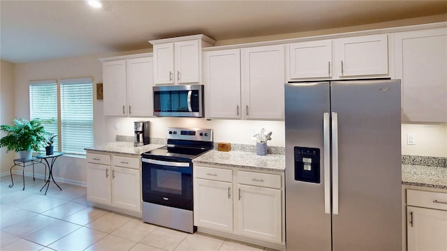 kitchen with light tile patterned floors, baseboards, light stone countertops, stainless steel appliances, and white cabinetry