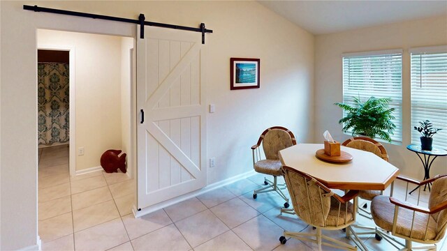 dining area featuring light tile patterned floors, a barn door, lofted ceiling, and baseboards