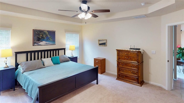 bedroom with multiple windows, a raised ceiling, visible vents, and light colored carpet