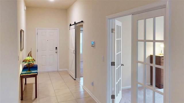 hall featuring light tile patterned flooring, baseboards, and a barn door