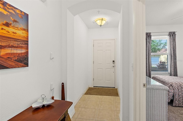 foyer entrance with arched walkways, light tile patterned flooring, and baseboards