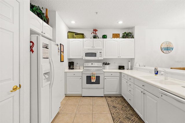 kitchen with light tile patterned floors, white appliances, a sink, and white cabinets