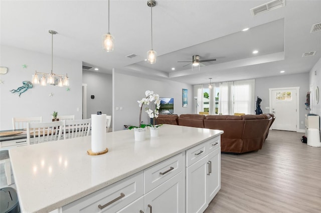 kitchen with white cabinetry, light wood-style flooring, visible vents, and a raised ceiling