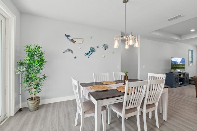 dining area with light wood-type flooring, a raised ceiling, visible vents, and baseboards