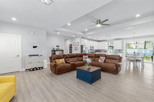 living area featuring light wood-style floors, recessed lighting, a raised ceiling, and baseboards