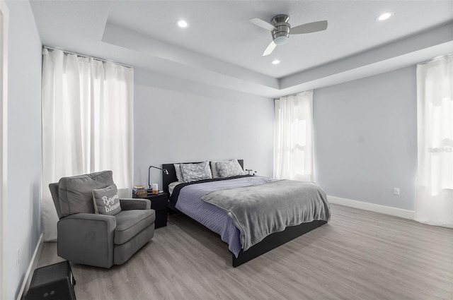 bedroom with baseboards, a tray ceiling, wood finished floors, and recessed lighting