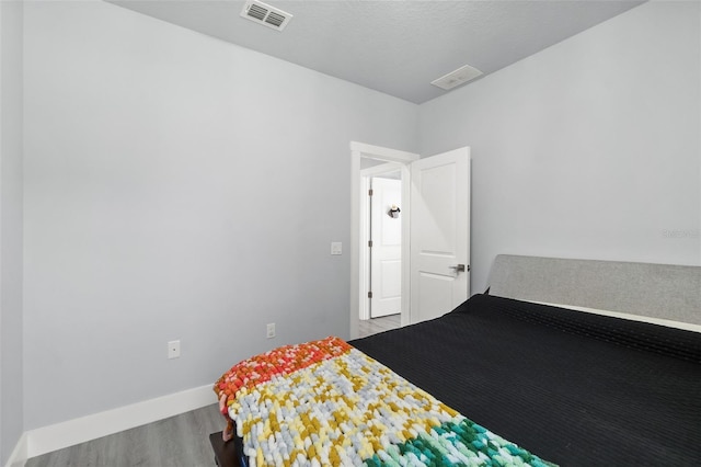 bedroom featuring a textured ceiling, wood finished floors, visible vents, and baseboards